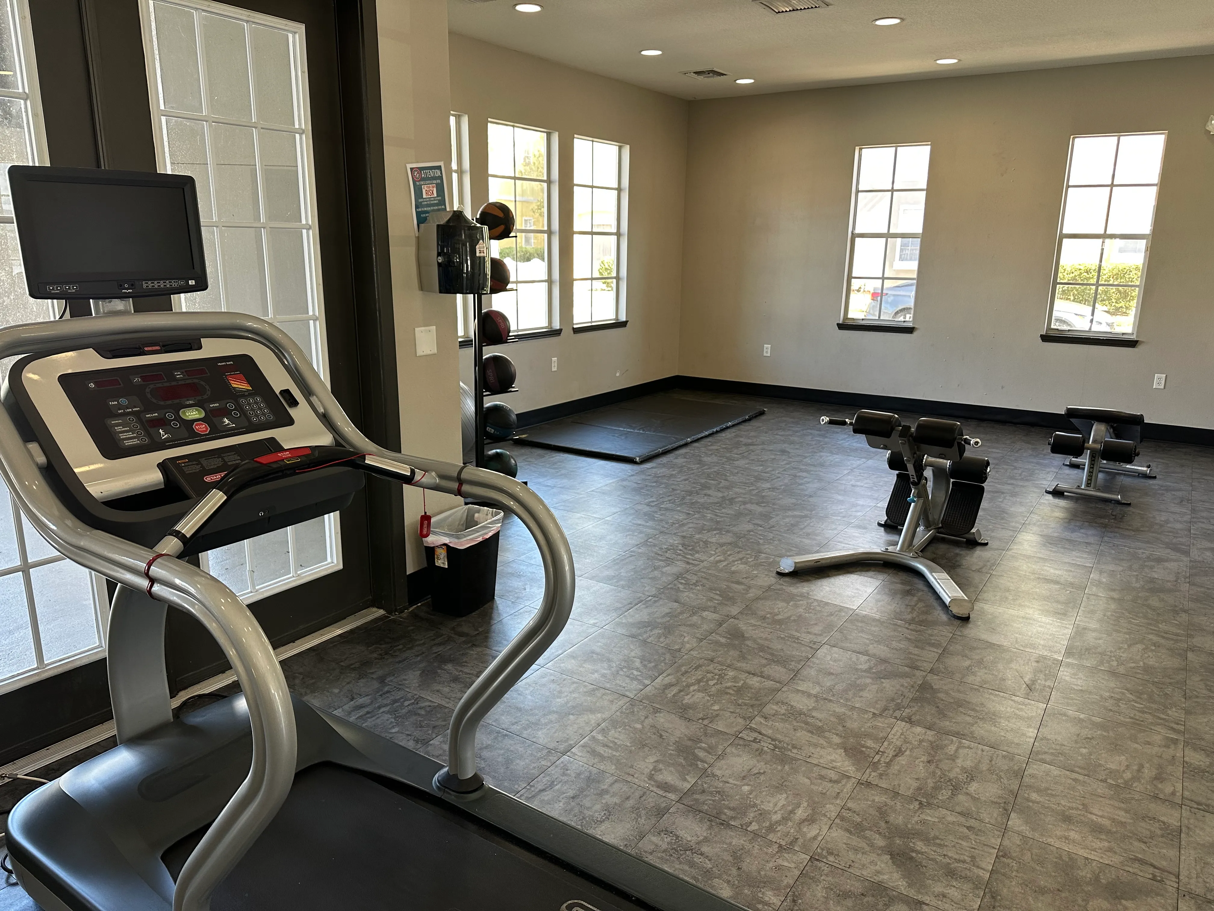 A treadmill with a monitor and control panel in a spacious gym with other exercise equipment.